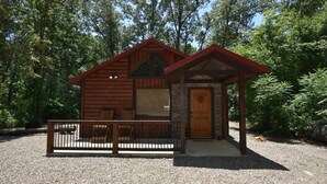 A rustic wooden cabin with a porch, a stone entrance, and a gravel driveway. - Lucky Log (Broken Bow)