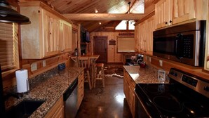A wooden cabin interior with a kitchen featuring granite countertops, a stove, a microwave, and wooden cabinets. - Lucky Log (Broken Bow)