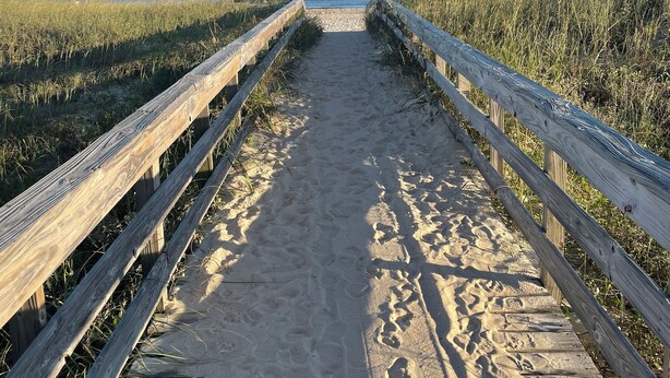 En træbro fører ned til en strand med klare himmel.