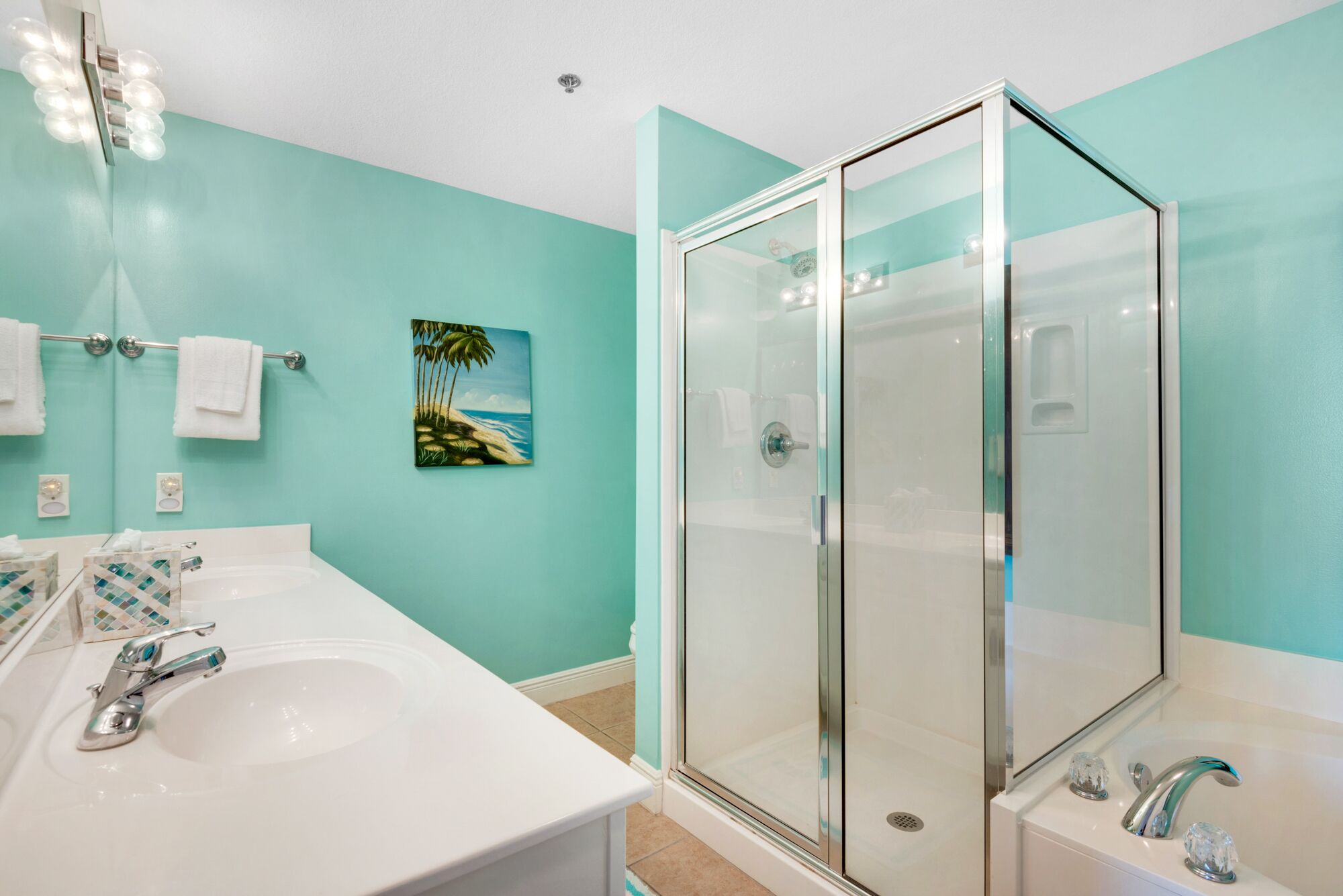 A modern bathroom with a glass shower enclosure, a white sink, and a painting of a beach scene.