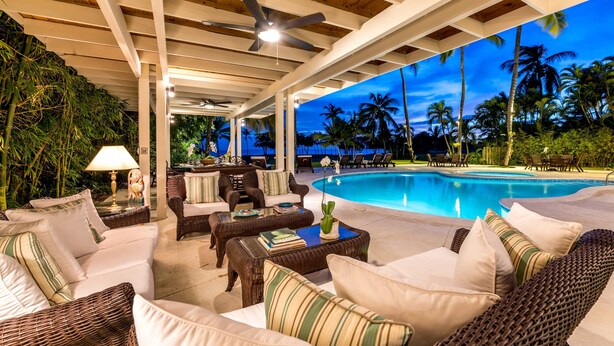 A covered outdoor seating area with wicker furniture, a pool, and a view of palm trees and the ocean at dusk. - Oceanfront, On Golf Course, Next to Beach, heated pool & hot tub, fully staffed (La Romana, CASA DE CAMPO)