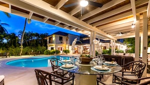 An outdoor dining area with a glass table, wicker chairs, and a pool in the background. - Oceanfront, On Golf Course, Next to Beach, heated pool & hot tub, fully staffed (La Romana, CASA DE CAMPO)