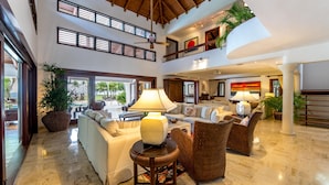 A spacious lobby with a high ceiling, a central seating area with sofas and armchairs, a large potted plant, and a view of the outdoors through large windows. - Oceanfront, On Golf Course, Next to Beach, heated pool & hot tub, fully staffed (La Romana, CASA DE CAMPO)