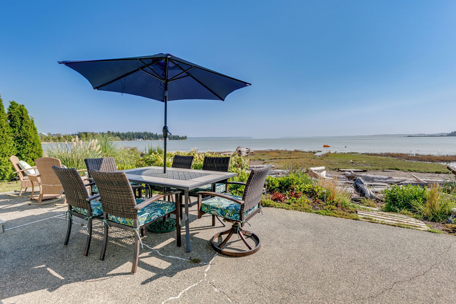 An outdoor patio with a table and chairs, a large umbrella, and a scenic view of a lake and distant land.