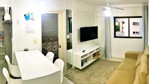 A living room with a TV, sofa, dining table, chairs, and a ceiling fan. - Vacanze - edf. Gales de Pajuçara apt 204, rooftop pool and gym. (Ponta Verde)