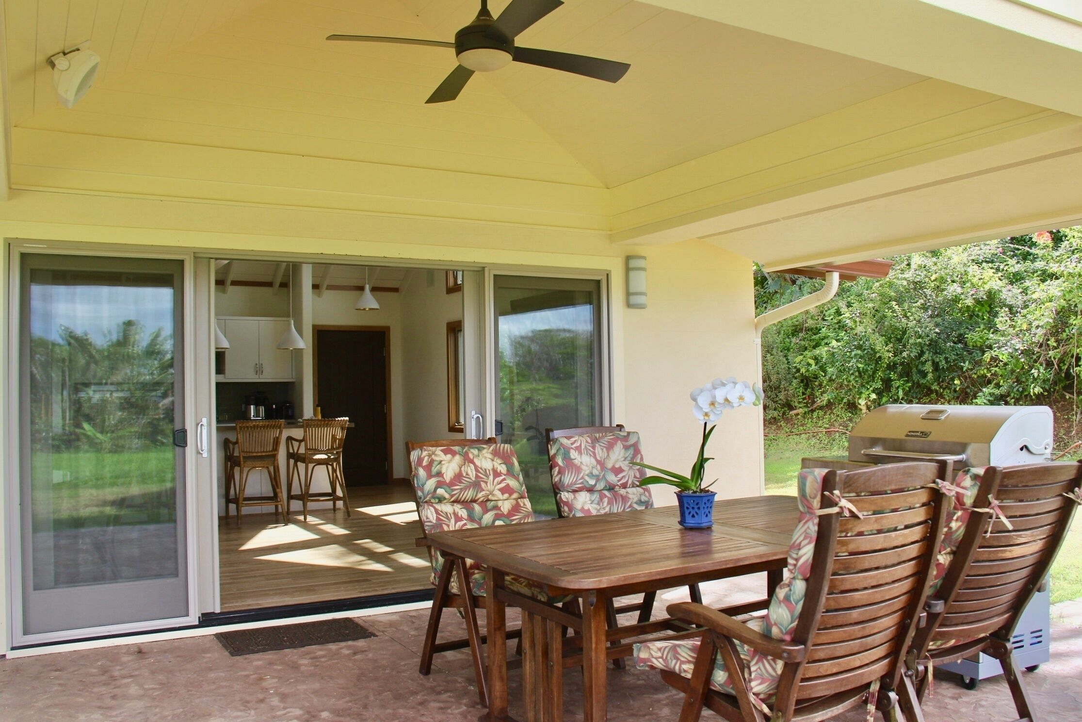 A covered patio area with a table and chairs, a ceiling fan, and a grill.