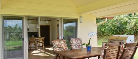 A covered patio area with a table and chairs, a ceiling fan, and a grill.