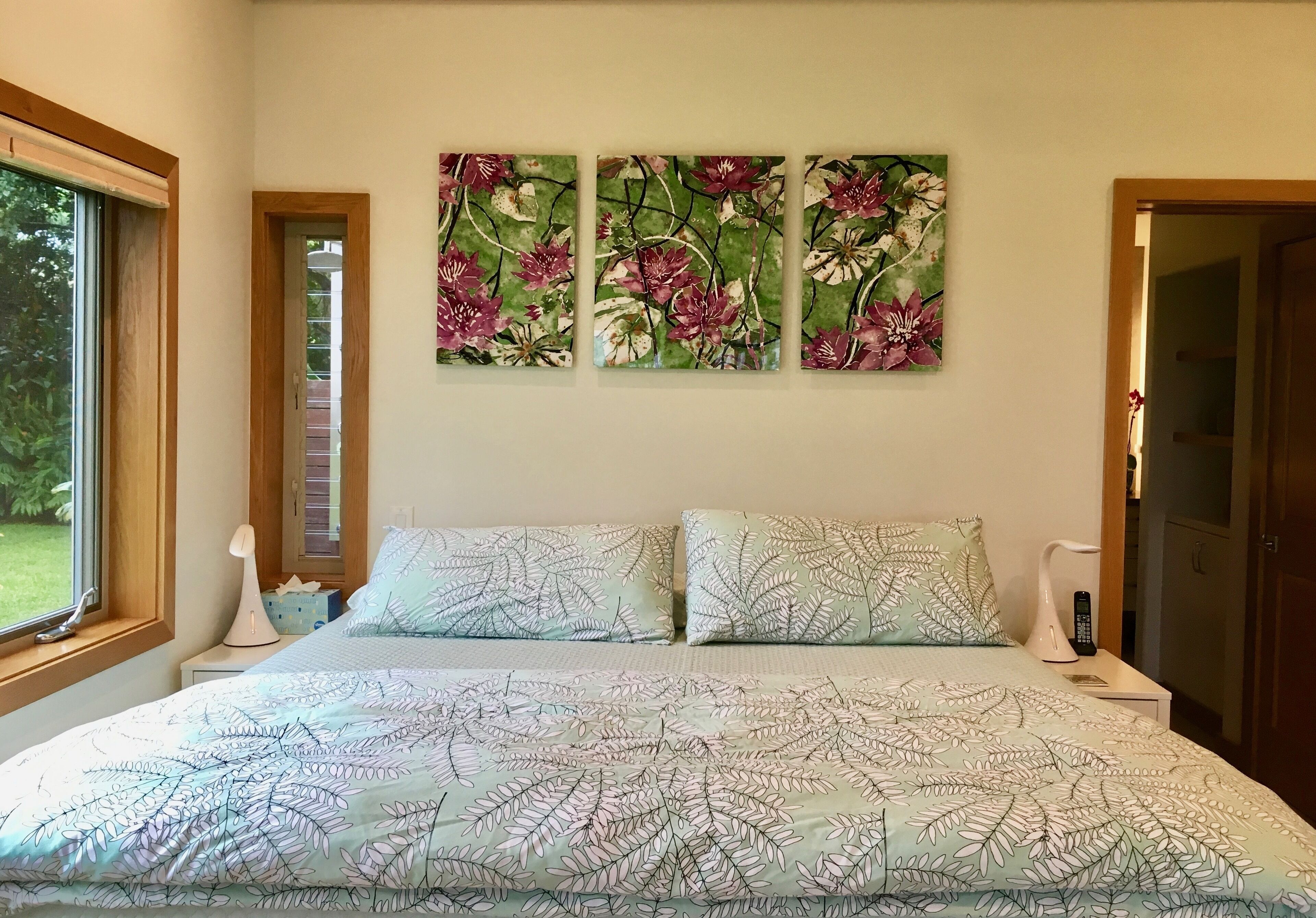 Un dormitori amb un llit, obra d'art floral a la part superior i una finestra a l'esquerra.