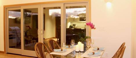Un coin repas avec une table en verre, des chaises en osier et une vue sur l’extérieur grâce à une porte-fenêtre coulissante.