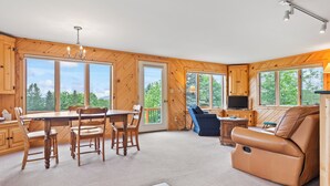 Une pièce spacieuse avec une table et des chaises en bois, un canapé en cuir et de grandes fenêtres donnant sur l’extérieur.