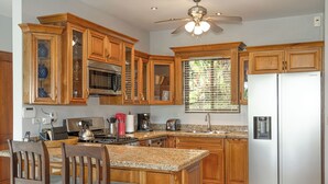 A kitchen with wooden cabinets, a stainless steel refrigerator, and a granite countertop. - Private Rainforest Retreat with Infinity Pool & Concierge (Quepos)