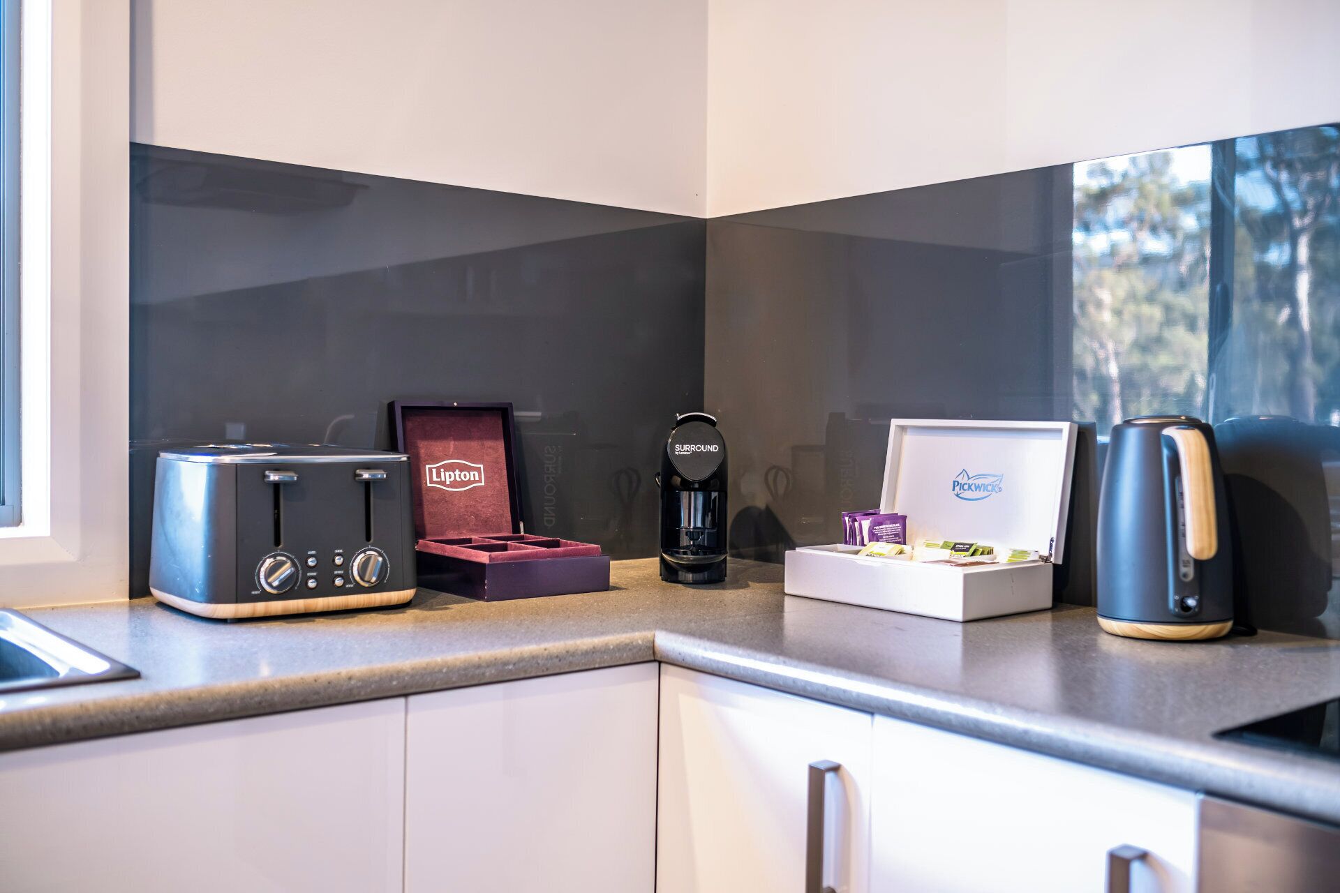 Un plan de travail de cuisine avec un grille-pain, une machine à café, une boîte de thé et une boîte de café.