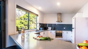 A modern kitchen with a large island, stainless steel appliances, and a view of greenery outside. - Harbour Master - Freycinet Holiday Houses (Coles Bay)