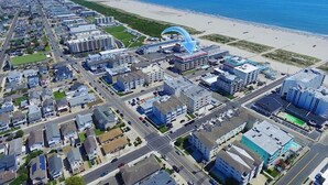 Luftaufnahme einer Küstenstadt mit Strand, die eine Mischung aus Wohn- und Geschäftsgebäuden, Straßen und einem wolkenlosen, blauen Himmel zeigt.
