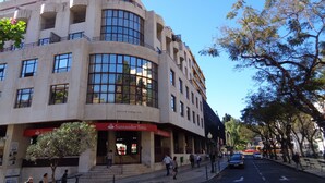 A modern building with a curved facade, large windows, and a visible entrance with a sign. - Superb View Over the Marina Funchal 270º view (Funchal)