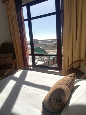 Une chambre d’hôtel avec une grande fenêtre, un lit sur lequel est posée une serviette roulée, et une chaise.