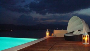 A poolside area with a lounge chair and two lanterns. - Breathtaking mediterranean view, large private infinite Pool & Jacuzzi ! (Theologos)