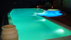 An infinity pool with illuminated edges, a stone urn, and a view of the sea at night. - Breathtaking mediterranean view, large private infinite Pool & Jacuzzi ! (Theologos)