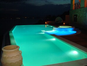 An infinity pool with illuminated edges, a stone urn, and a view of the sea at night. - Breathtaking mediterranean view, large private infinite Pool & Jacuzzi ! (Theologos)