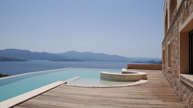 A infinity pool with a wooden deck and a stone building. - Breathtaking mediterranean view, large private infinite Pool & Jacuzzi ! (Theologos)