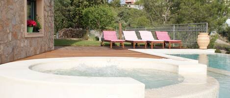 Un espace piscine comprenant un jacuzzi, une terrasse en bois et des chaises longues.