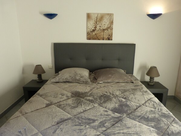 Une chambre à coucher comprenant un lit, deux lampes de chevet, une tête de lit et un luminaire fixé au mur.