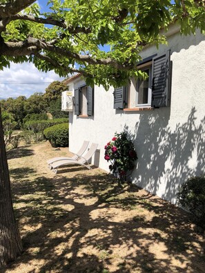 Un bâtiment blanc avec des volets, un jardin avec un banc et un arbre.