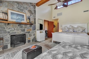 A bedroom with a stone fireplace, a bed with patterned bedding, a wooden chest, and a ceiling fan. - Spectacular Views, Close to everything Rehoboth + Pet Friendly! (Rehoboth Beach)