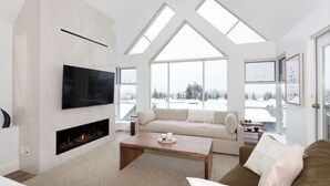 A spacious living room with a fireplace, a large flat-screen TV, a sofa, and a coffee table. - LUXURY- 2BA/BA True Ski-in/Ski-out, HotTub&Pool (Whistler)