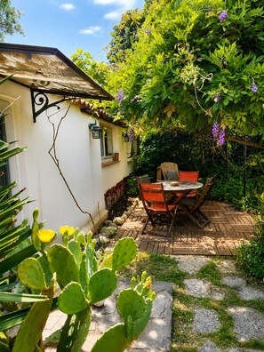 Eine Terrasse mit Tisch und Stühlen, umgeben von Pflanzen und einer Kaktee.