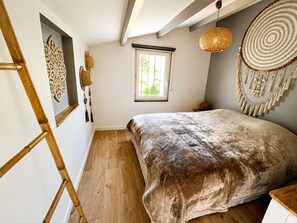Ein Schlafzimmer mit einer Holzleiter, einem Bett mit strukturierter Decke, einem Fenster mit Blick und dekorativen Wandgestaltungen.