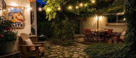 A patio with stone flooring, wooden furniture, and string lights.