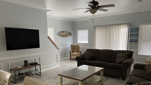 Una sala de estar con un televisor de pantalla plana, un ventilador de techo, un sofá, una mesita de centro y un sillón.