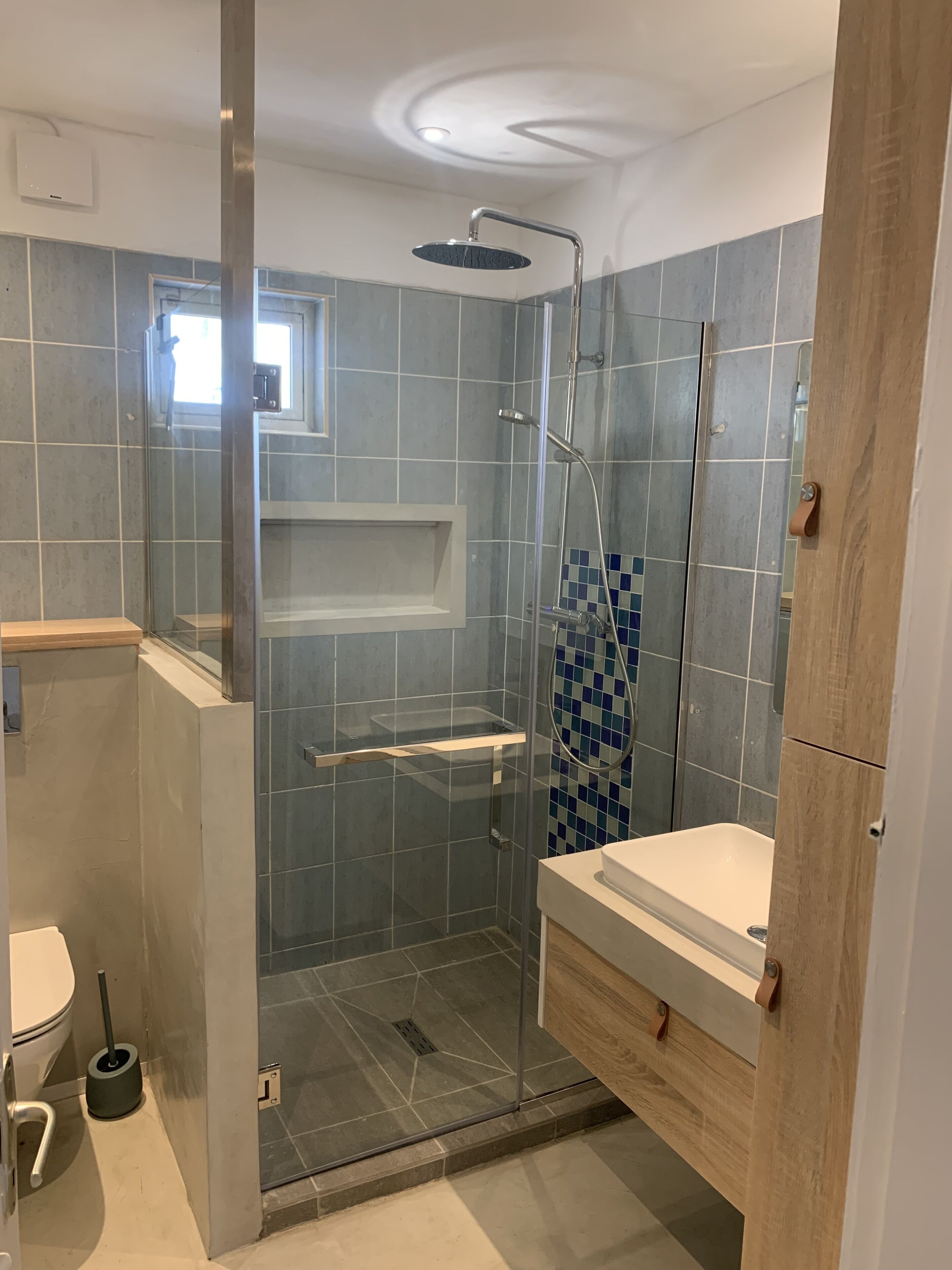 Un baño moderno con ducha de vidrio, lavamanos blanco y tocador de madera.