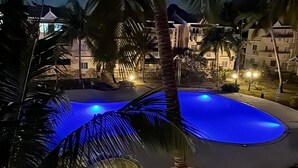 A nighttime view of a swimming pool surrounded by palm trees and buildings. - Superb apartment-300m from beach (Rate incl. free WiFi, maid service, parking..) (Flic en Flac)