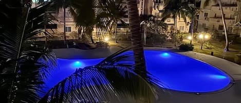 A nighttime view of a swimming pool surrounded by palm trees and buildings.