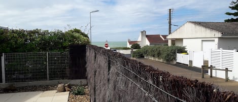 A coastal residential area with a paved walkway, a metal fence, and a view of the sea.