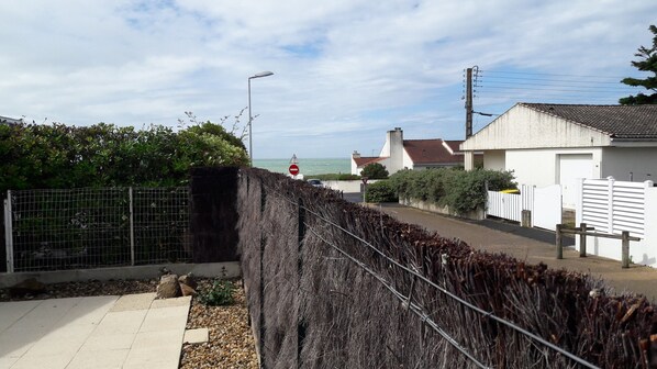 A coastal residential area with a paved walkway, a metal fence, and a view of the sea.