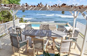 Un área de estar al aire libre techada con piscina y vista al océano.