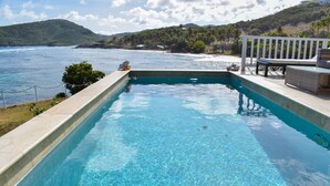Una piscina rectangular de agua cristalina y azul, rodeada por una terraza blanca y muebles de mimbre.