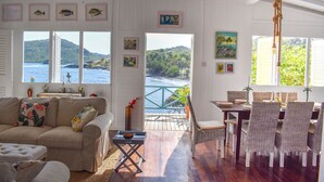 Un salon chaleureux avec vue sur l’océan, un coin repas avec des chaises en osier et une terrasse en bois.