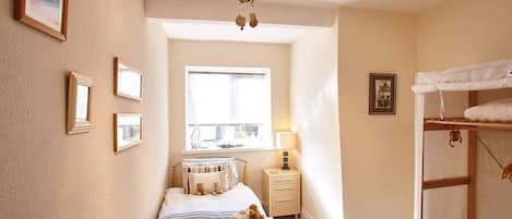 Une chambre à coucher avec un lit, une table de chevet, une lampe, une fenêtre, un lit superposé et des tableaux encadrés accrochés au mur.