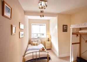 A bedroom with a bed, bedside table, lamp, and a bunk bed.