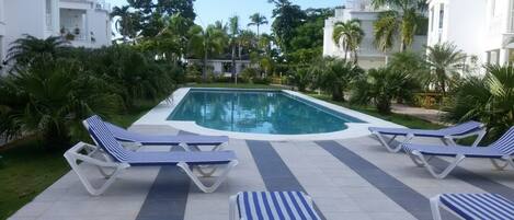 A swimming pool with lounge chairs and palm trees.