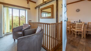Une pièce spacieuse avec une grande fenêtre, une table à manger en bois avec des chaises, un canapé gris et une rambarde en bois.