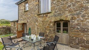 Un bâtiment en pierre doté d’un patio comprenant une table et des chaises, une porte et une fenêtre.