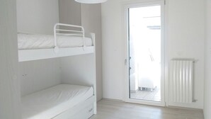 Une chambre avec des lits superposés, un radiateur blanc et une porte donnant sur un balcon.