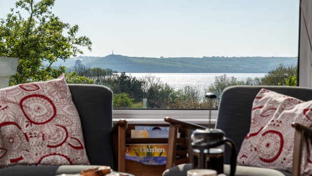 A table with breakfast items, a coffee pot, and a view of a lake and hills. - Schoopers is set amongst rolling green fields on the edge of the Camel Estuary. (Wadebridge)