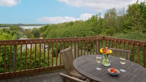 A wooden deck with a round table, two chairs, a vase with flowers, and two glasses of white wine. - Schoopers is set amongst rolling green fields on the edge of the Camel Estuary. (Wadebridge)