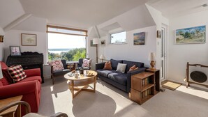 A living room with a red sofa, a dark blue sofa, a wooden coffee table, and a bookshelf. - Schoopers is set amongst rolling green fields on the edge of the Camel Estuary. (Wadebridge)